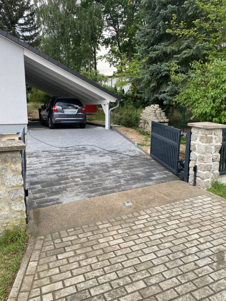 Metalleinfahrtstor von JD-Zaun Jakub Dunowski vor einem Haus mit schön verlegtem Pflasterstein