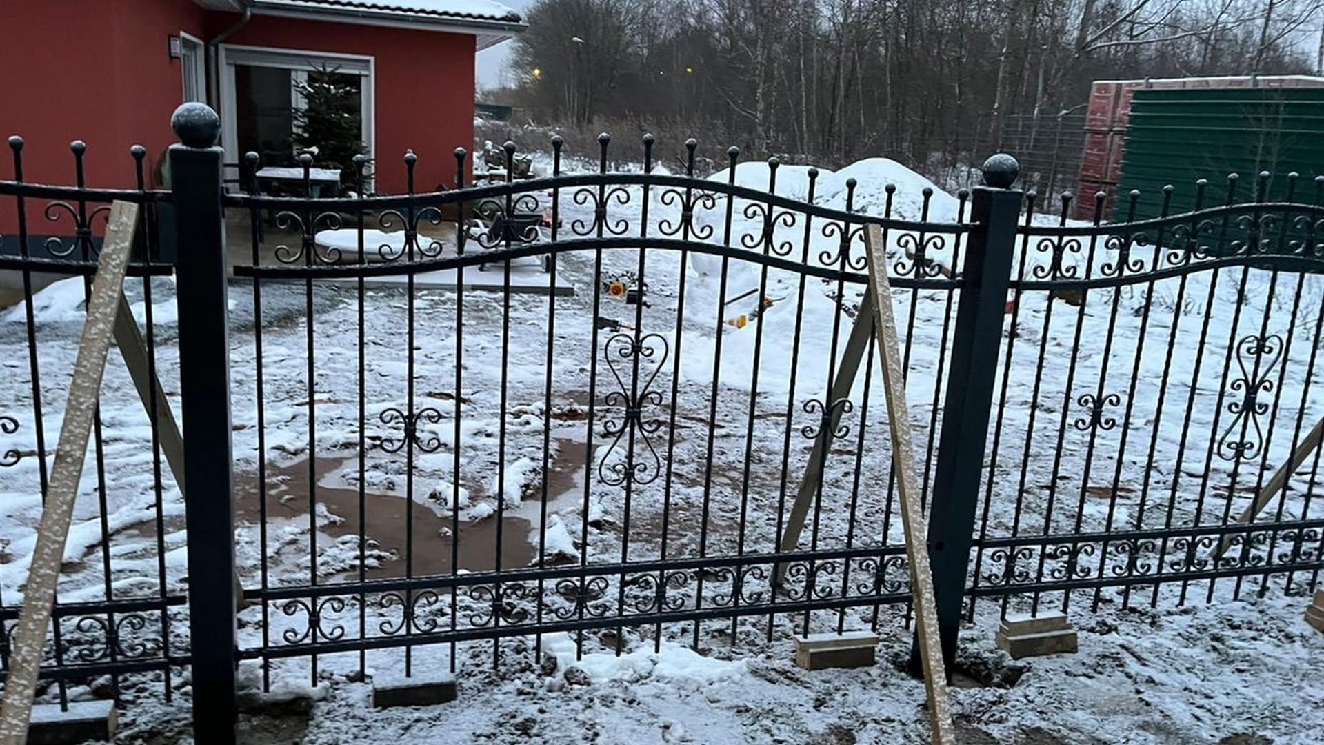 Schmiedeeisernes Tor mit Schnee und rotem Haus.