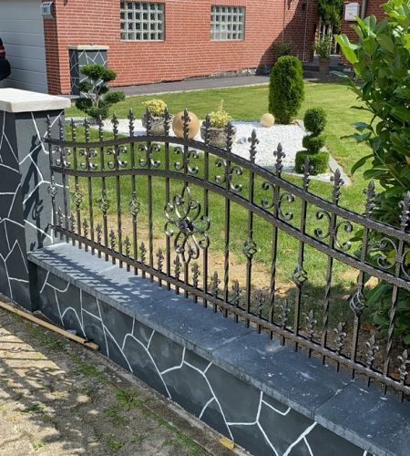 Dekorativer Metallzaun von JD-Zaun mit kunstvollen Verzierungen, eingebettet in eine gepflegte Gartenumgebung