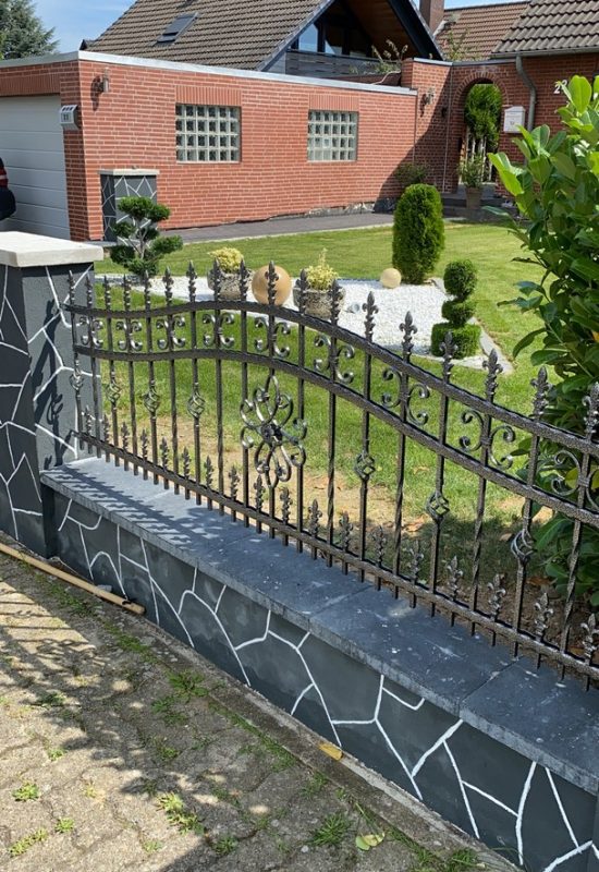 Dekorativer Metallzaun von JD-Zaun mit kunstvollen Verzierungen, eingebettet in eine gepflegte Gartenumgebung