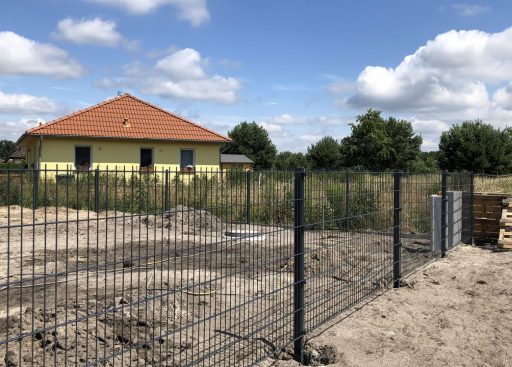 Neue Doppelstabmattenzaun von JD-Zaun, die ein Grundstück umgeben, mit einem gelben Haus im Hintergrund